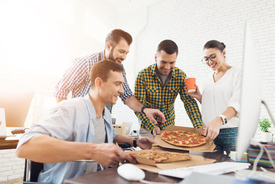 Office workers and man in a wheelchair are eating pizza. They work in a bright and modern office.