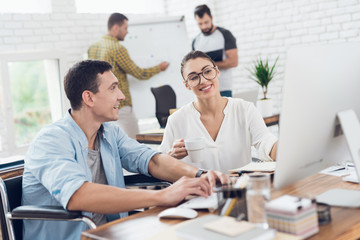 A man in a wheelchair is making a conversation with a girl. They are working in a bright office.