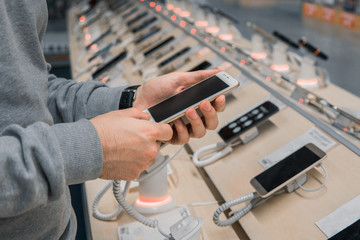 Closeup view of male customer hands, choosing white smartphone in the mobile phone store. difficult decision. Various choice