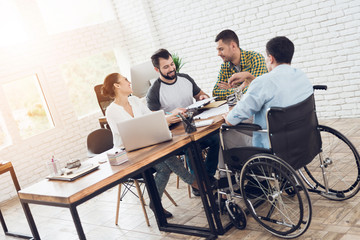Office workers and man in a wheelchair are making a conversation in bright office.