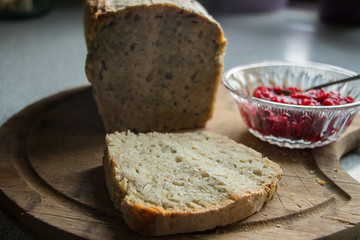 Homemade bread with pips lying on a wooden board with a glass bowl of homemade raspberry jam