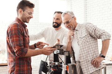 Three men set up a self-made 3d printer to print the form. They are checking the 3d model of the tablet.