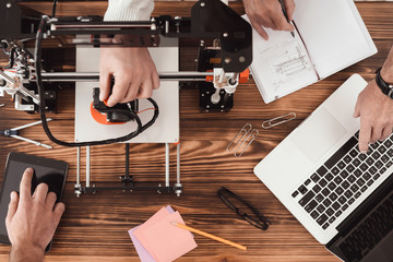Three men are working on creating a 3d printer. Teamwork. One of the men works with a computer.