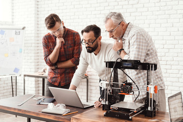 Three men are working on preparing a 3d printer for printing. One of them explains the rest of the subtlety the print.