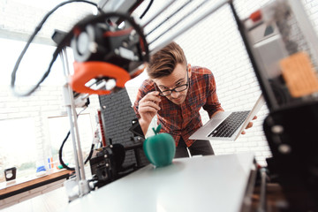 A man with a laptop in his hands controls the process of printing a 3d printer. 3d printer has printed model of an apple