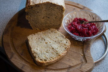 Homemade bread with pips lying on a wooden board with a glass bowl of homemade raspberry jam