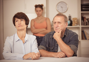 Upset female and her husband are sitting at the table and their daughter is sympathying with them