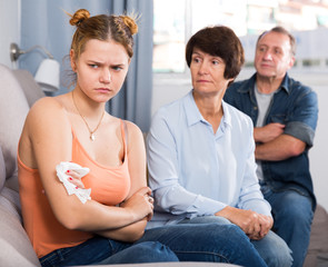 Adult couple is carefully talking with a sad daughter on sofa