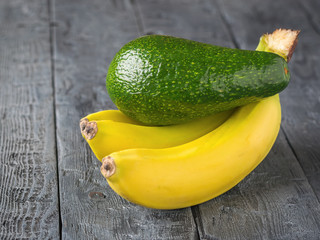 Ripe juicy fruits of banana and avocado on rustic wooden table.