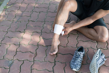 Sports injury. Asia young man runner is rewinding ankle bandage. Man with pain in ankle