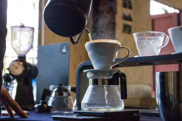 Close-up Hand drip coffee pouring water on coffee ground with filter On a wooden desk at coffee shop