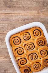 Fresh homemade cinnamon buns in a white baking dish. Copy space . Wooden background. 