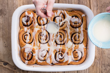 The process of glazing cinnamon buns. Hand motion. Wooden tabletop. 