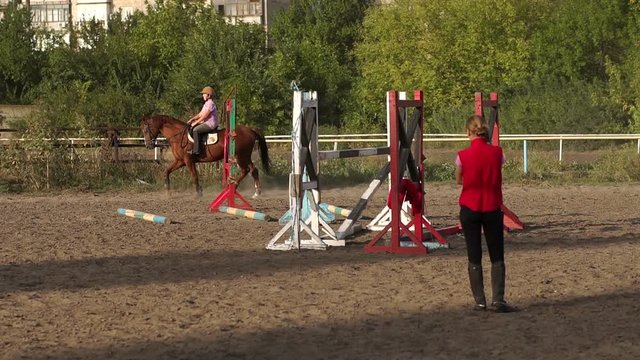 A teenage girl is engaged in horse riding under the supervision of a coach. Slow motion. Wide shot.