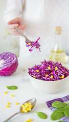 Fototapeta na wymiar Salad of red cabbage and corn. Woman's hand holds fork with salad