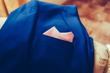Expensive men's blue jacket lying on the couch with a pink handkerchief in his pocket. Closeup. Vintage tonted photo.