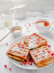 Delicious mouth-watering Viennese waffles with honey and pomegranate seeds on a white plate, light wooden background