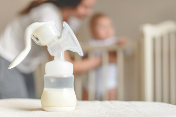 Manual breast pump and bottle with breast milk on the background of mother and baby near the baby's bed. - 181575857