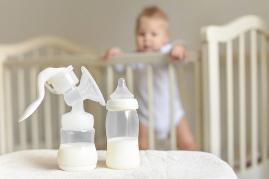 Manual breast pump and bottle with breast milk on the background of little baby in bed.