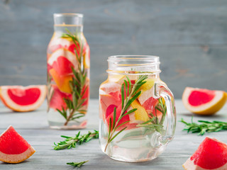 infused detox water with grapefruit and rosemary in mason jar and glass bottle on gray wooden table. diet healthy eating and weight loss concept, copy space for text