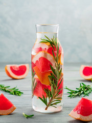 infused detox water with grapefruit and rosemary in glass bottle on gray wooden table. diet healthy eating and weight loss concept, copy space for text