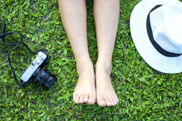 Top view of legs of bare foot Asian woman  sitting for relaxing with white hat and camera on a green grass, Hobby freetime and leisure time
