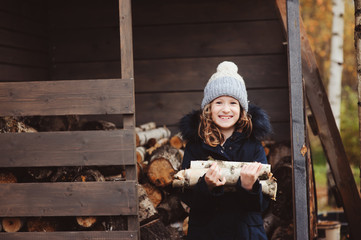 happy child girl picking firewood from shed in winter or autumn
