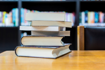 Stack of books in library   with burred book shelf background, selective focus.