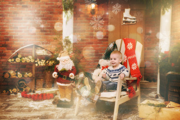 Fototapeta na wymiar Happy little child boy dressed in sweater sitting on the chair with Santa in decorated New Year room at home. Christmas good mood. Family and holiday 2018 concept. Magical highlight bokeh effect