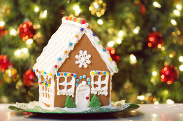 Homemade Christmas Gingerbread House displayed on a table. Decorated Christmas tree in the background.