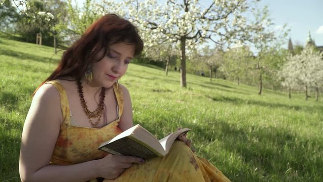 A woman reading a book while sitting on the grass in the Petrin park in Prague in Spring