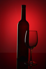 Bottle of wine and empty wine glass on red background