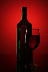 Green bottle and a glass of wine on a red background