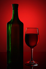 Green bottle and a glass of wine on a red background