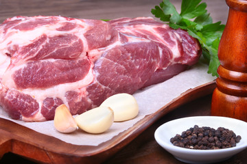 Raw pork neck chop meat with parsley herb leaves, grinder for spices and garlic on a stone background. Ready for cooking.