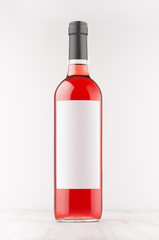 Rose wine bottle with blank white label on white wooden board, mock up, vertical. Template for advertising, design, branding identity.