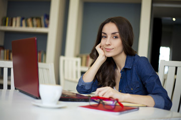 Close up portrait of beautiful smiling young brunette women while working at laptop in cafe