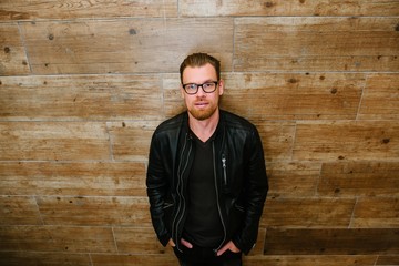 Handsome man in black jacket and glasses posing outdoor wooden wall. Men's beauty, fashion. Business-like style.