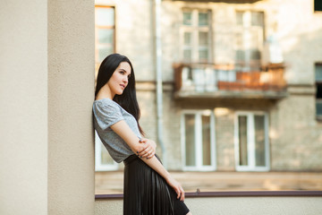 attractive young girl posing near building. slim woman in a gray shirt and a black leather skirt...
