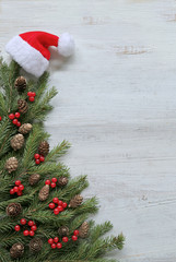 Christmas tree branches with red berries, gold cones on wooden background 