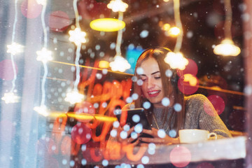 Young beautiful woman sitting in cafe, drinking coffee. Model listening to music. Christmas, Happy new year, Valentines day, winter holidays concept