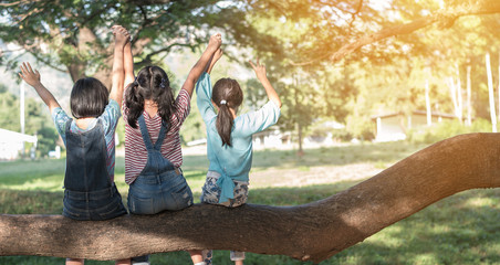 Children friendship concept with happy girl kids in the park having fun sitting under the tree...