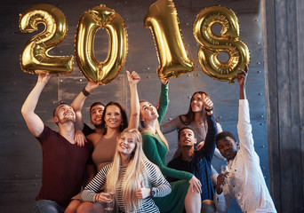 A group of merry young people hold numbers indicating the arrival of a new 2018 year. The party is dedicated to the celebration of the new year. Concepts about youth togetherness lifestyle