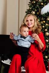 Happy beautiful young mother and her little one-year-old baby sitting on armchair