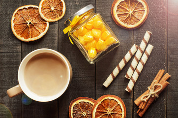 Hot chocolate, cinnamon sticks, oranges and candies on a dark wooden background, top view