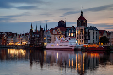 View of two boats and old buildings at the Long Bridge waterfront at the Main Town (Old Town) in Gdansk, Poland, in the evening.