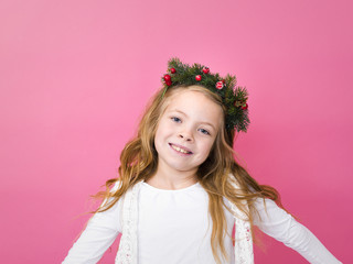 beautiful blond girl with christmas decoration on her head in front of pink background