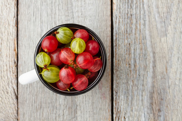 Green and red gooseberries in an enamel mug