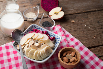 Bowl of oatmeal porridge with bananas, apple, dragon fruit and almonds. Top view