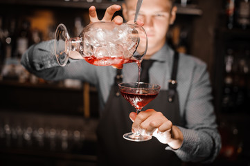 Barman pouring a red alcoholic cocktail into the glass